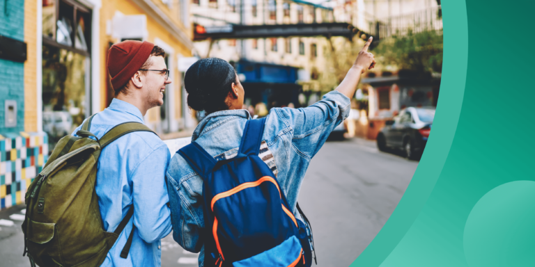 Two students walk along an urban street, wearing backpacks and fall clothing