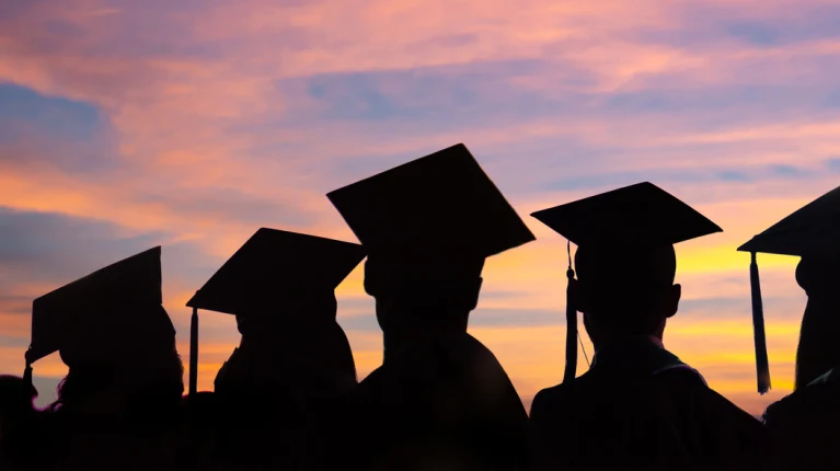 A photo of the silhouettes of graduates with a sunset in the back.
